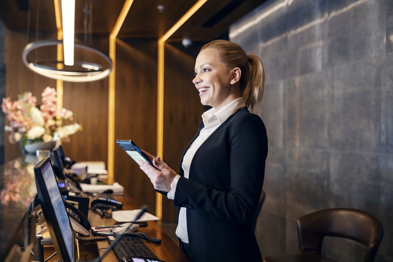 A hotel front desk clerk beams a smile at an incoming guest from behind a row of POS systems